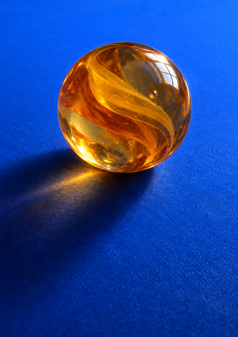 Large translucent amber-orange sphere with swirling internal bands, a small bubble, and bright reflection on a saturated blue ground.