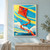 Large tilted red-orange kite with a blue patch and long tail flying over a turquoise and yellow sky, clouds, water, and wooded shore.; frame shown for styling only