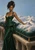 Woman in an emerald gown beside oversized green velvet cushions topped with clouds and snowy miniature mountains.
