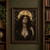 Dark-haired woman wearing layered gold necklaces before a large full moon, framed by shadowy serpentine coils.; frame shown for styling only