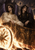 Two crowned winged figures in pale and black robes sit in a gold chariot beside flames beneath a dark sun.