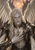 A long-haired winged man in black-and-silver armor beneath a star-like light and between dark spires.
