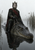 Crowned dark-haired rider in black and red sits astride a large crocodile in shallow, reed-lined marsh water.