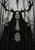 Dark-haired woman in black with raised hands touching branching antlers against a distressed monochrome forest-like background.