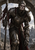 Pale armored figure in a pointed helmet beneath a broken stone arch, holding a tall staff or spear beside a coiling snake.