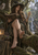 Woman in a pointed hat seated in a forest with an open book, green glow, owl, distant stag, and waterfall.