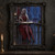 Silver-haired gray-skinned elf in a red gown writes with a quill at an ornate black desk, with silver threads and a blue spider-decorated hall behind her.; frame shown for styling only