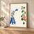 Small pale robot on a blue step stool watering a drooping green houseplant on a wall shelf. in a styling frame; frame not included