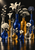Cluster of clear, cobalt and amber glass vessels holding pale flowers and leafy stems on a reflective surface against a dark background.