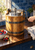 Wooden ice-cream churn with metal bands and side crank on a kitchen counter beside berries and a folded towel.
