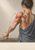 Anatomy illustration of a clothed adult figure reaching for a ceramic vessel, with exposed shoulder and back musculature and three arrows.