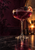 A dark ruby drink with bubbles in a coupe, garnished with a blackberry and citrus slice beside an amber candle.