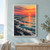 Coral-orange sun and broken reflection over teal tidal flats, with sweeping shoreline bands, a distant ridge, and two small wading birds.; frame shown for styling only