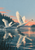 Two ivory swans rise from a reflective lake, with a wooded shoreline and low coral-pink dawn light behind them.