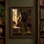 Fluffy black cat with copper eyes reaching toward a hanging red ribbon beside a green chair, open book, and sunlit shelves.; frame shown for styling only