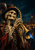 A hat-wearing skeleton plays a brass trumpet angled toward the lower right, with a blue glow at the bell and amber carnival lights behind.