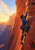 A blue-clad climber reaches upward on a steep red sandstone wall beside a sunlit canyon opening.