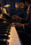 Adult male pianist in profile at an upright piano, one hand on the keys and one raised, lit by a blue-shaded lamp and amber window.