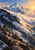A snowy alpine peak rises above dark conifer-dotted ridges and a cloud-filled valley lit by warm sunlight.