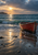 Weathered red rowboat partly cropped at the right edge, resting in shallow surf above reflective wet sand with a low headland and sunlit clouds.