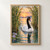 White-bodied black-necked swan gliding between tall reeds on reflective sunset water, with lavender flowers at lower left.; frame shown for styling only