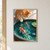 Ginger tabby cat leaning over a round teal pond, watching a red-and-white koi below while one white paw hovers above the water.; frame shown for styling only