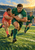 Green rugby ball carrier runs toward the viewer with an oval ball as a coral-clad defender reaches behind and a teammate supports at right.