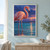 A coral-pink flamingo with an S-curved neck and a droplet at its bill stands in turquoise water; two flamingos are distant beneath a violet-blue sky.; frame shown for styling only