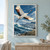 White crane with a red crown flying above blue coastal surf, with a smaller bird near the distant shore.; frame shown for styling only