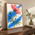 Large coral-pink flower with a dark magenta center on curved stems, narrow leaves, buds and detached petals against a cobalt brushstroke and warm-white background.; frame shown for styling only