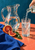 Hand pours water from a bottle into a tall tumbler beside a clear pitcher, blood-orange halves, leaves, and cobalt cloth.