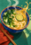 Overhead view of a cobalt bowl with an orange rim filled with lime-topped noodle broth, beside chopsticks and a rust-red napkin.