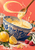 Pale batter loops from a wooden spoon into a blue-and-white patterned mixing bowl, surrounded by lemons, raspberries, eggs, flour and leaves.