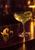 Golden cocktail in a coupe glass with two olives on a pick, citrus peel, and a loose olive on a reflective dark bar.