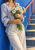 Cropped figure holding white daisies with yellow centers and green stems, wearing a blue-and-white striped shirt beside a blue wall and coral stair rail.