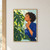 Adult woman with short dark curls holding a glass mister beside large split leaves, with “SUNROOM PAUSE” lettering at the bottom.; frame shown for styling only