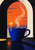 Oversized cobalt cup with curling steam beneath an arched orange-red sunset window, above a dark counter with a long blue-violet shadow.