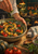 Hands scattering herbs over a rustic bowl of roasted squash, tomatoes, and greens beside a striped towel and wooden spoon.