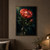 Open coral protea with a side bud and glossy dark leaves in a small glass vase against a near-black teal background.; frame shown for styling only