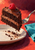 A raspberry-topped slice of layered chocolate cake lifted on a silver fork above a white plate against a coral-red background.