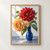 Red and golden-apricot dahlia-like blooms with a smaller blush flower and green leaves in a cobalt-blue vase on a blue-gray tabletop.; frame shown for styling only