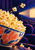 A coral-and-blue patterned bowl overflowing with popcorn, kernels arcing toward a projector beam in a dark theater.