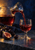Clear carafe pouring red wine into a stemmed glass beside dark grapes and a cut fig on a dark blue tabletop.