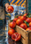 Red-orange citrus piled in a wooden crate, with a hand holding an orange above a halved ruby-fleshed fruit and a striped market canopy behind.