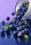 A tipped white enamel bowl spills blueberries, leaves, and droplets across a reflective dark-blue surface; a cut berry sits in front.