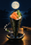 Upright nori hand roll filled with salmon, cucumber, and rice on a black plate, with chopsticks, loose rice, and a moonlit seascape.