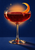 Ruby-red cocktail in a coupe glass with a crescent-shaped orange peel, set against an indigo background with an apricot glow.