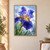 Large blue-violet bearded iris with a golden throat, ruffled petals, raindrops, and green leaves against a pale blue background crossed by fine rain streaks.; frame shown for styling only