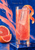 Pink grapefruit drink in a tall glass with curled citrus peel and grapefruit slices against cobalt blue; “Pomelo Hour” appears above.