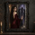 Woman in a burgundy gown touching an ornate mirror with three dark veiled figures visible in its shadowy reflection.; frame shown for styling only